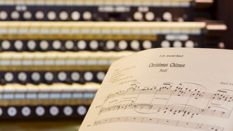 Closeup of an organ keyboard with sheet music for Christmas Chimes Noel in the right foreground.