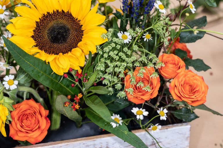 A floral arrangement featuring a bright yellow sunflower and other fall flowers.