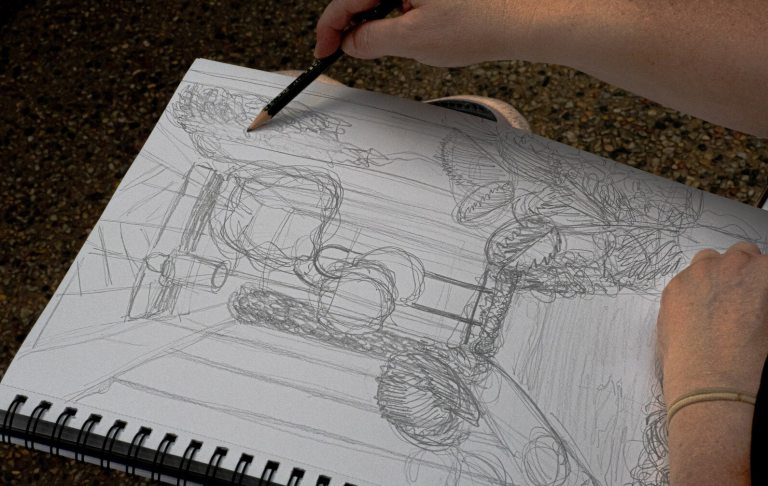 A persons hands, holding a pencil, sketching an indoor garden.