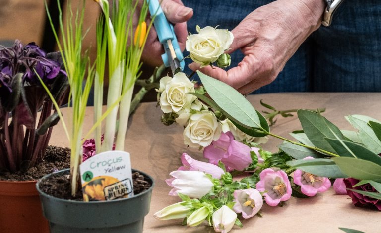 A person's hands holding scissors while creating a spring floral arrangement.
