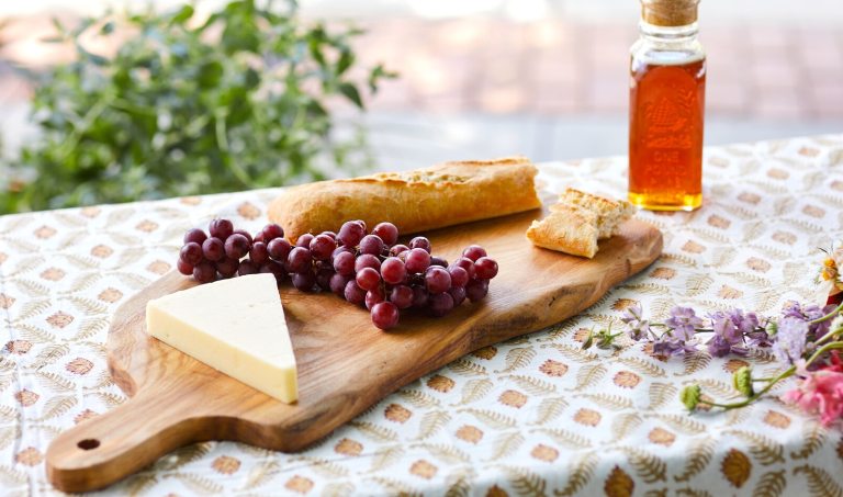 A cheese board featuring a wooden board, different cheese types, and grapes.