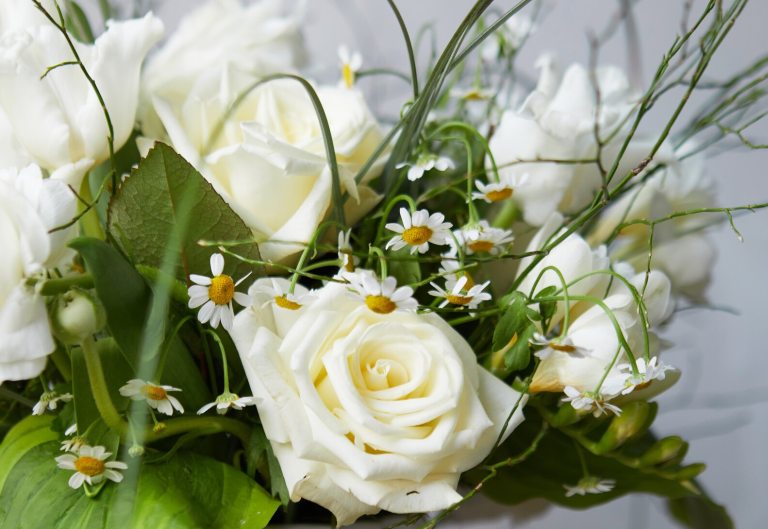 An floral centerpiece featuring white roses and green foliage.