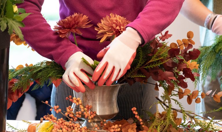 A person creating a floral arrangement in a silver vase.
