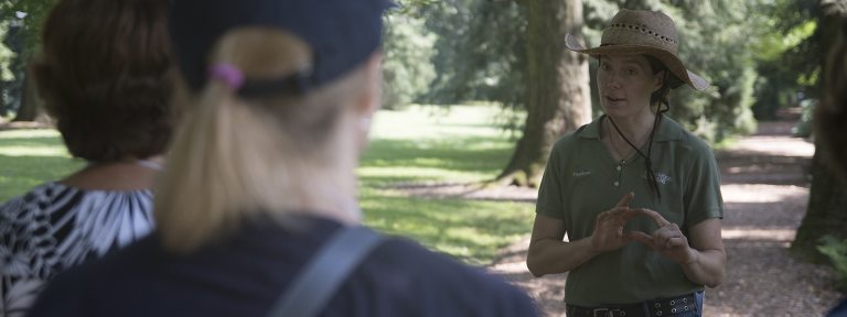 a person in a straw hat speaks to other people in a garden setting