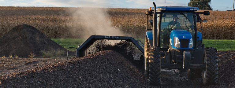 A blue tractor processes rows of compost in a field 