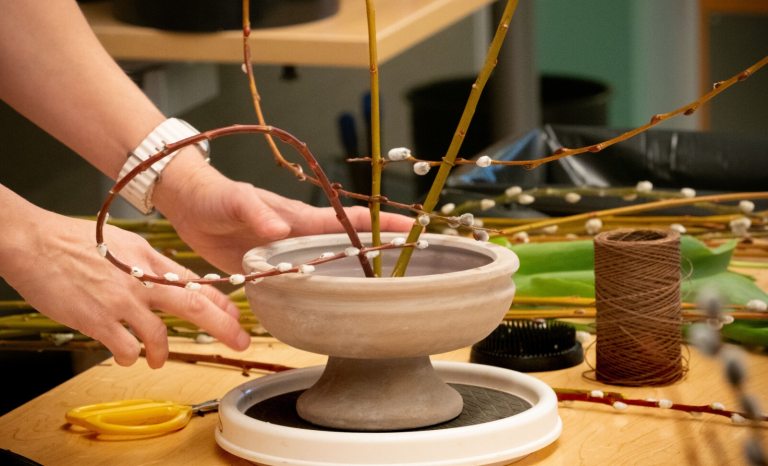 A person creating a floral arrangement out of pussy willow branches.
