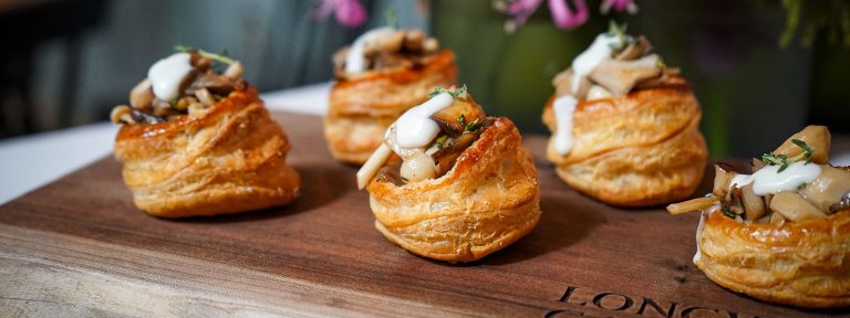 Six pastry appetizers on a wooden board, ready for serving.