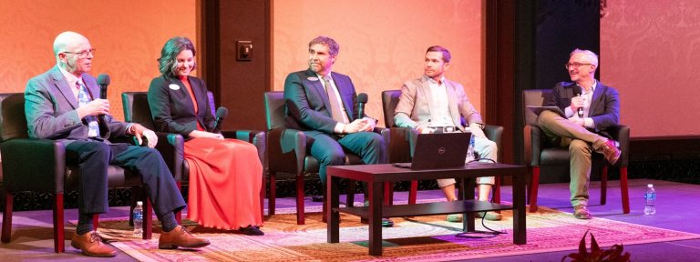 A panel of people, sitting on a stage, in a row looking at an audience.