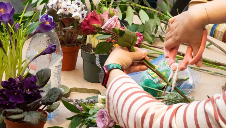 A person using scissors to cut a flower stem while crafting a floral arrangement.
