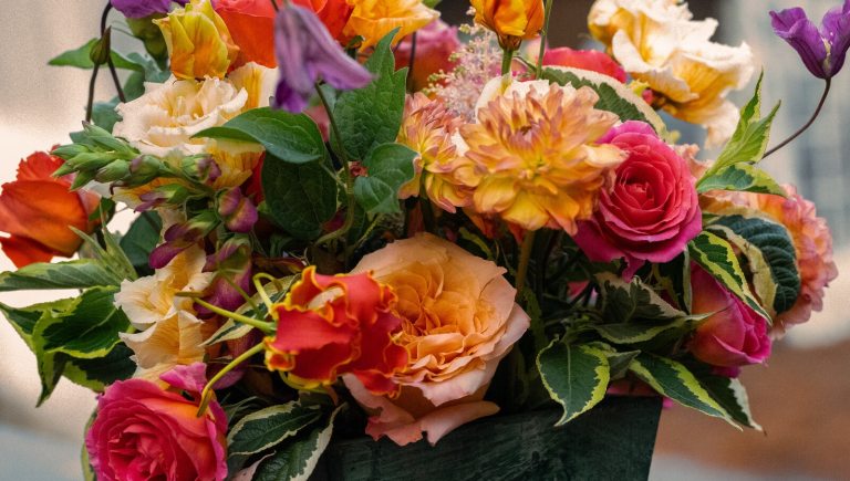 A bright and lush flower arrangement featuring dahlias, roses, and green foliage.