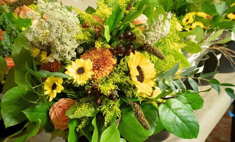 A late summer floral arrangement featuring green foliage, sunflowers, and peach blooms.