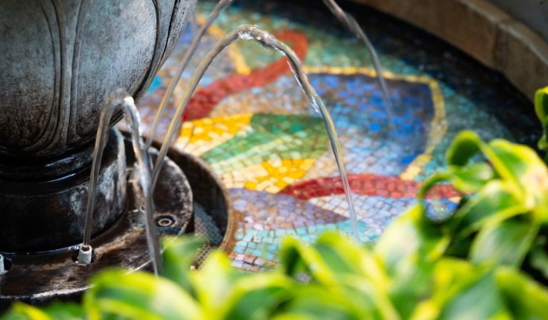 A small fountain with water going into a mosaic tile basin.