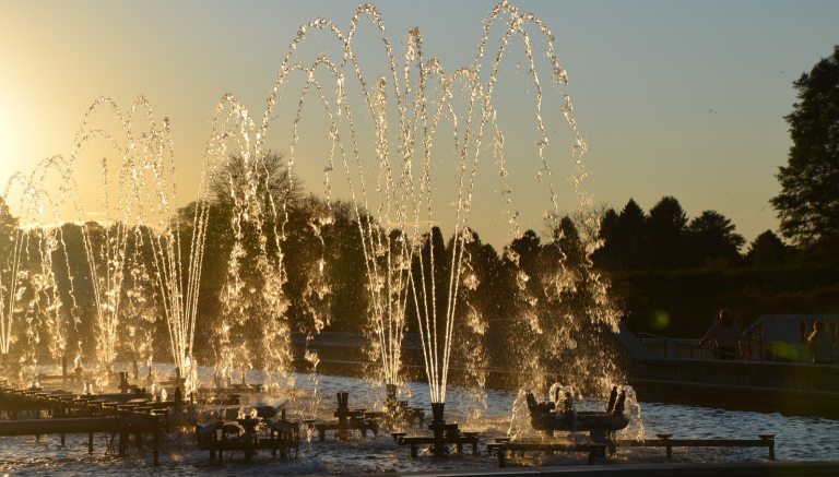 A row of fountains, spraying water up in the air, at sunset.