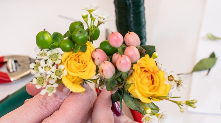 A persons hand creating a floral arrangement out of yellow and pink flowers.