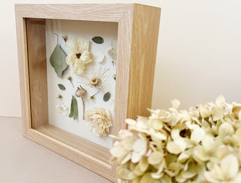 Shadow box frame with pressed and dried flowers and dried hydrangea stem in foreground
