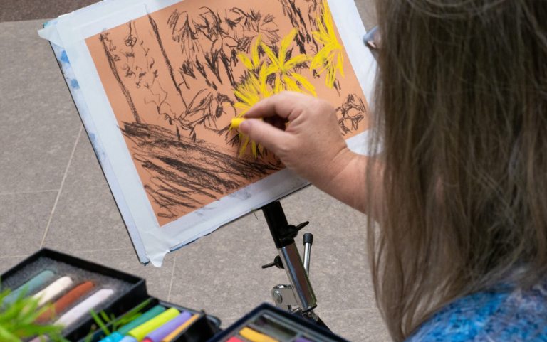 A person using pastels to create a piece of art inspired by an indoor plant conservatory.