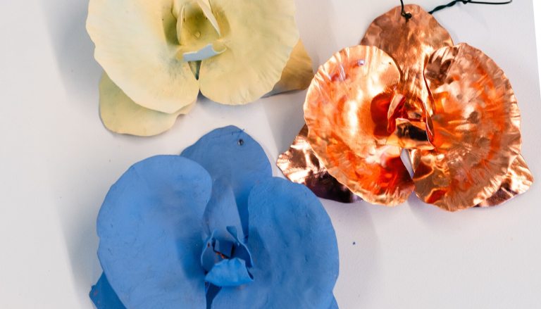 Three copper ornaments, two painted in white and blue, in the shape of an orchid, on a white background.