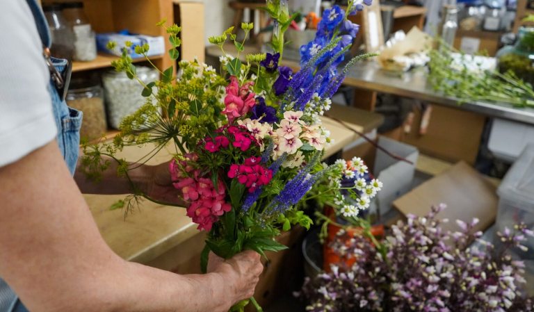 A person creating a floral arrangment frompink and purple flowers.