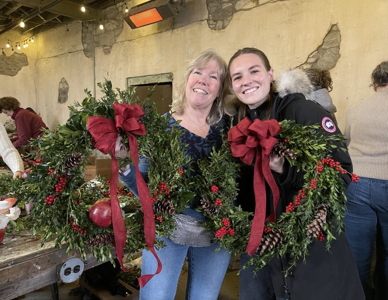 Two women smiling and holding holiday wreaths.