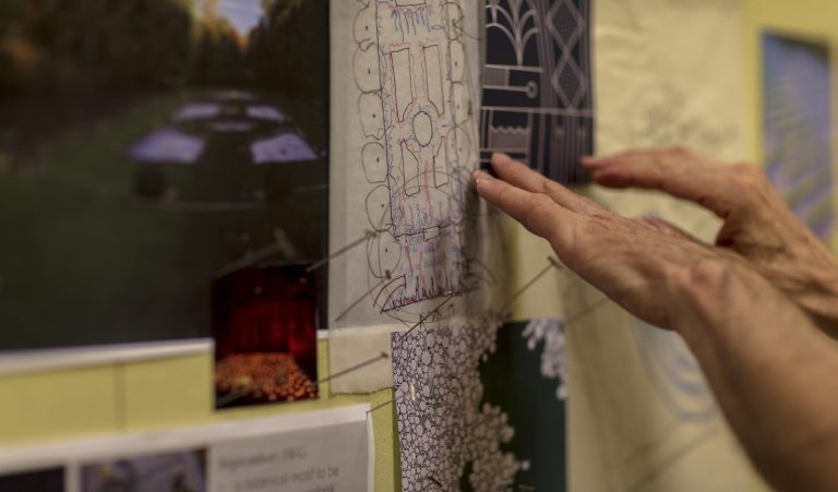 A person's hands pointing at landscape design plans hanging on a wall.