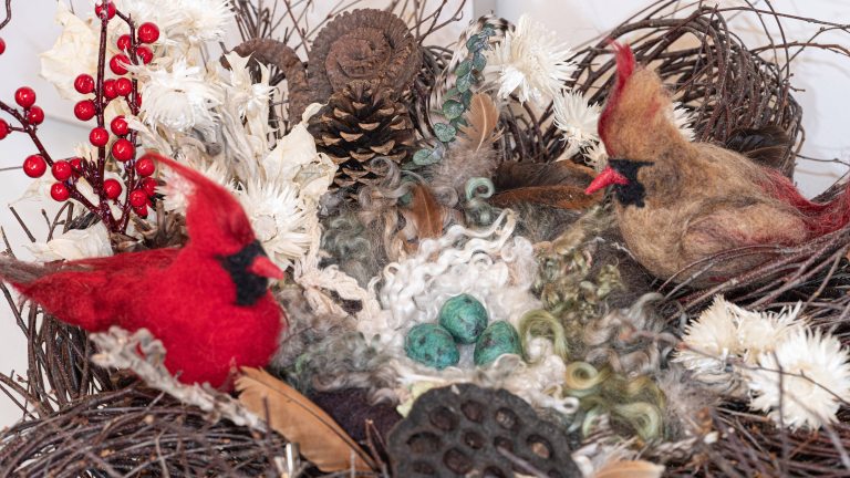 Two felt cardinals, male and female, sit in a nest of natural materials.