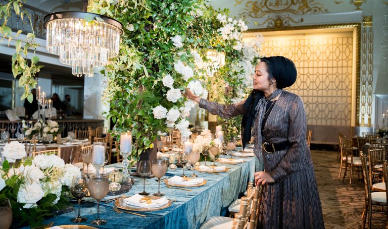 A person arranging a floral centerpiece next to an elegantly set table. 