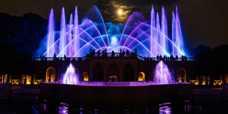 Purple and blue fountains rise beneath a full moon.