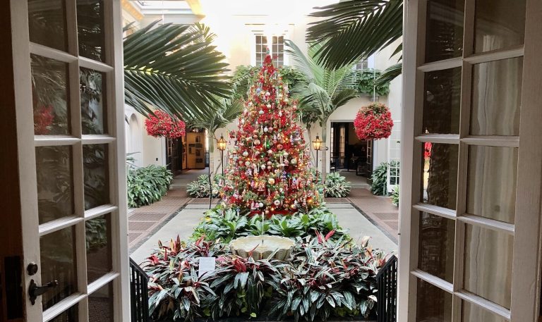 The view through french style doors, opening to a conservatory with a red and gold decorated christmas tree in the center.