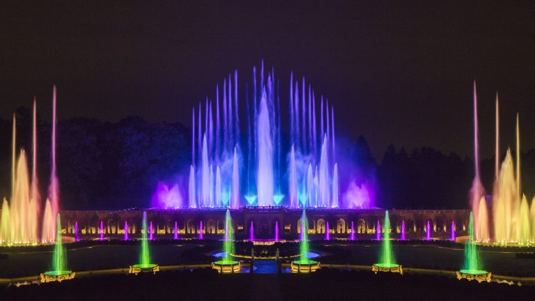 Evening in the Main Fountain Garden, with multi-colored jets of water in green, blue, purple, yellow and colors in between shooting into the dark sky