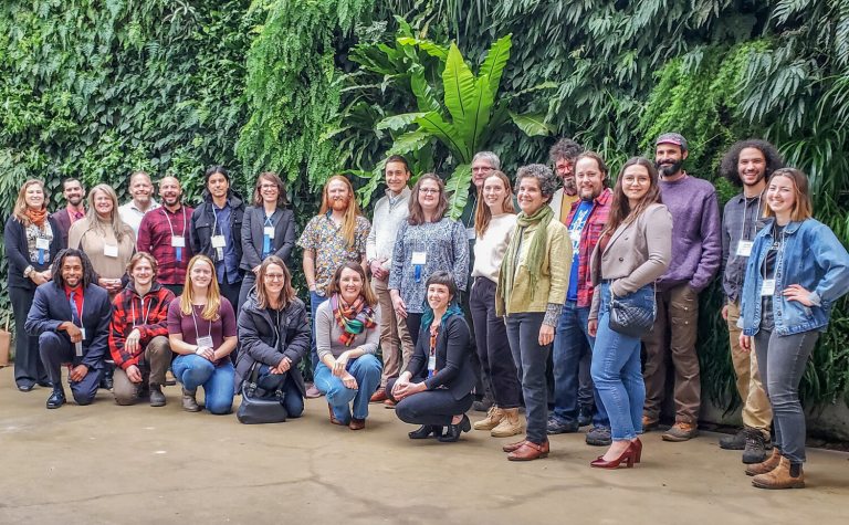 A large group of people standing in two rows, in front of the green wall at Longwood Gardens.