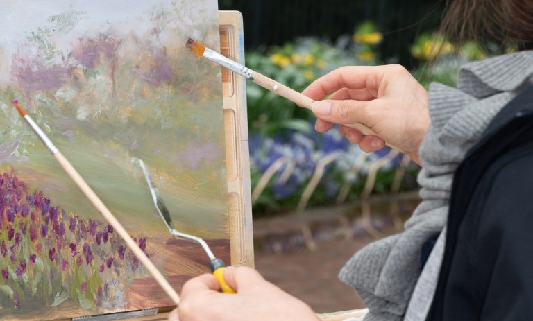 A person using paintbrushes to create a still life painting.