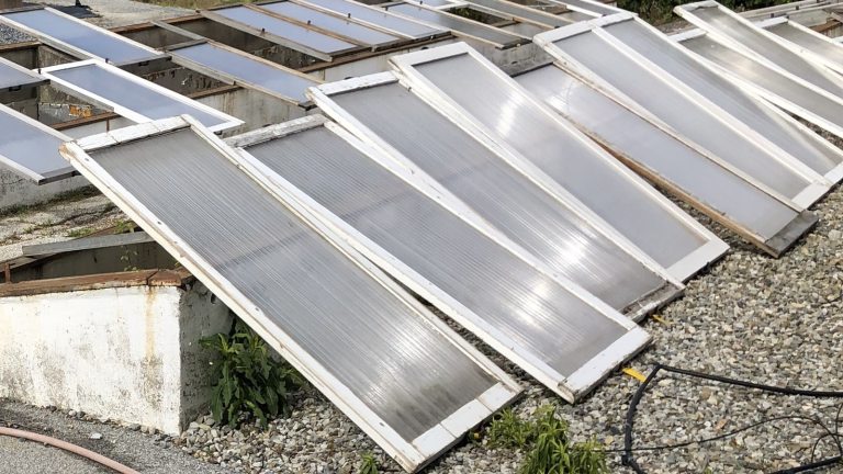 An outdoor, high-angle view of multiple cold frames, lying at a slight angle on a rough, gravel-covered ground or rooftop. 