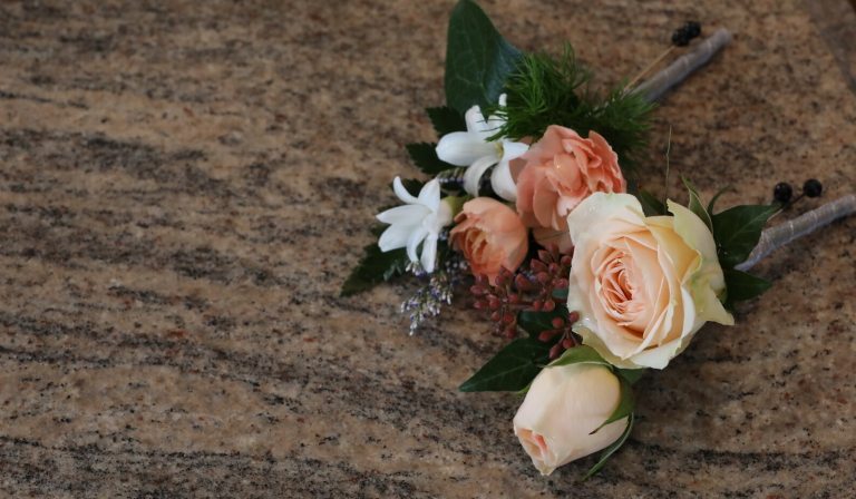 Two small floral lapel pieces laying on a wood graid table.