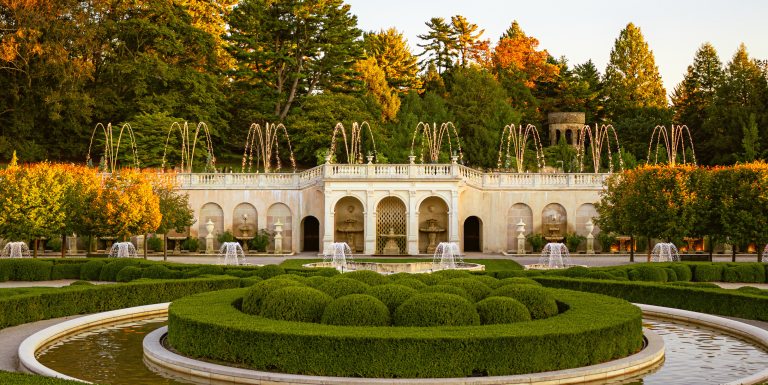 Arched stone fountain facade, with fountains rising amid changing autumn foliage.
