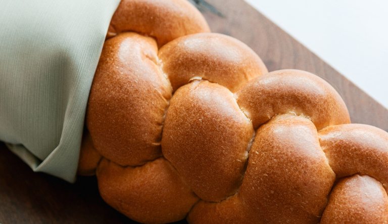 A close-up, high-angle view of a golden brown, freshly baked loaf of braided bread.