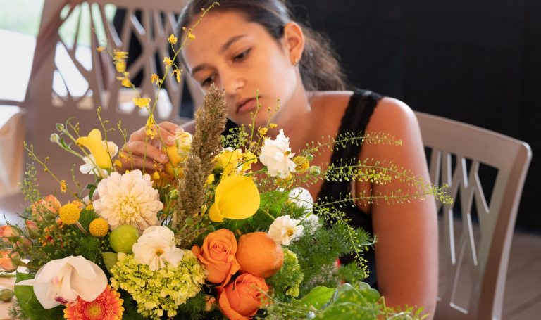 A person creating a floral arrangement seated at a table.