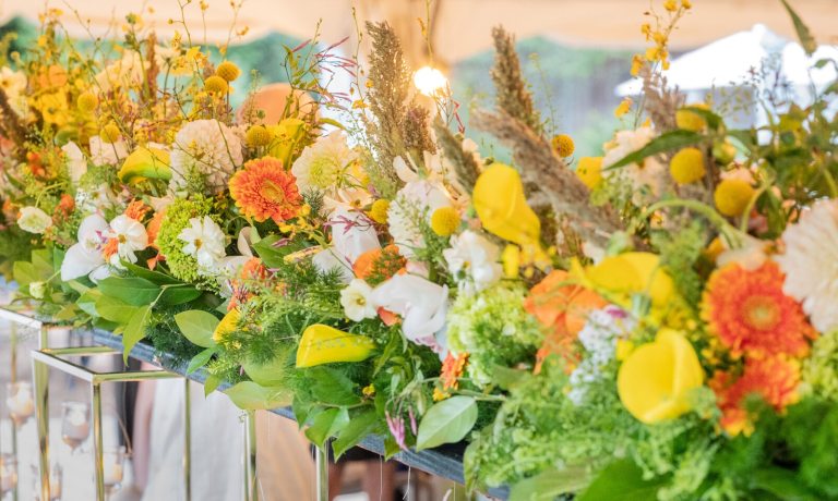 A tablescape of yellow, orange, and white flowers in tall mirrored vases.
