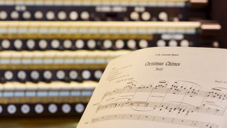 Closeup of an organ keyboard with sheet music for Christmas Chimes Noel in the right foreground.