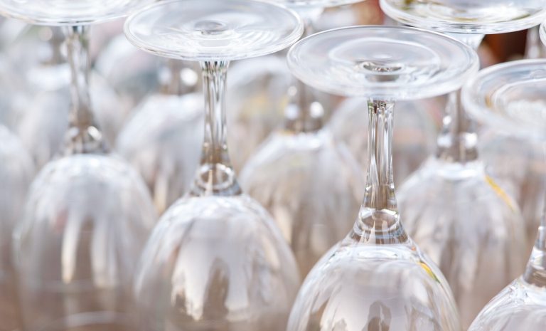Rows of clean wine glasses inverted, showing the rounded bowl of the glass pointing up and the flat base pointing down, ready for an event.