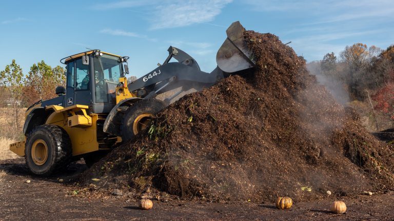 A yellow tractor on a steaming pile of dark brown composted soil.