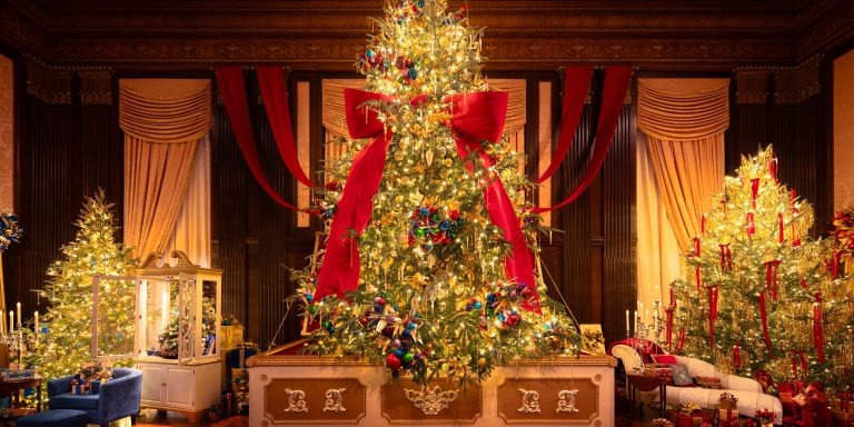 A tall indoor Christmas tree, tied with a giant red bow, seems to arise from a music box, flanked by two smaller trees.