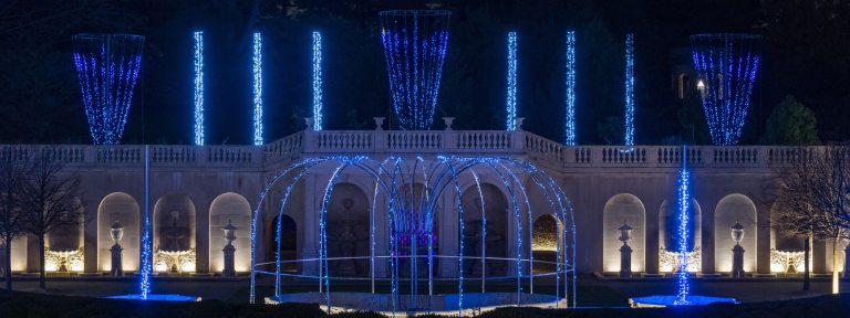 Wide view of fountain garden with fountain jets of blue light instead of water.