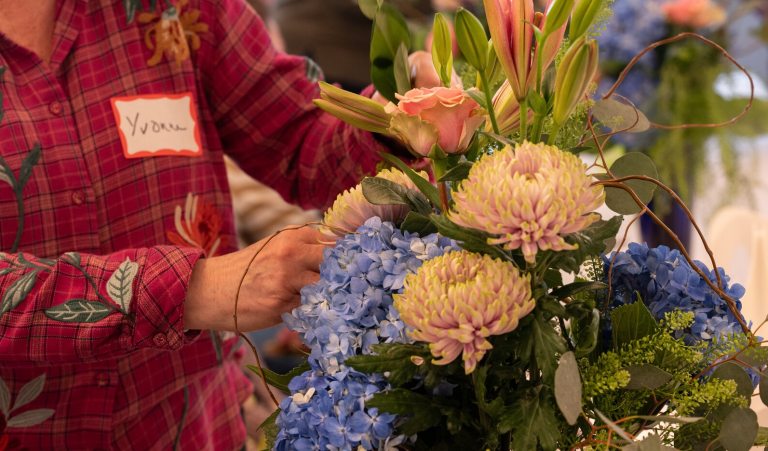 A person in a red plaid shirt creating a floral design with white and blue flowers.