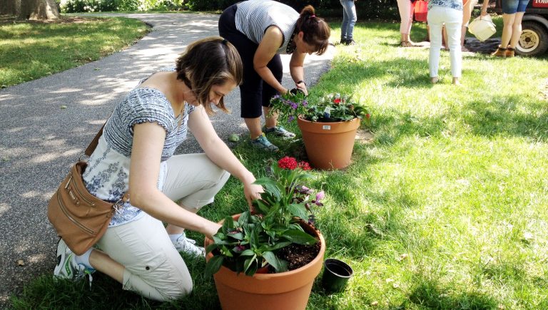 Two woman plant flowers in terra cotta containers.