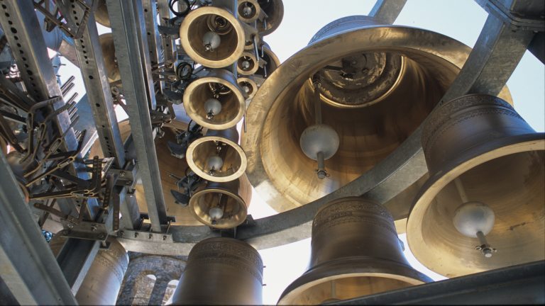 View from below of large and small carillon bells, awaiting installation into stone tower visible at bottom left.