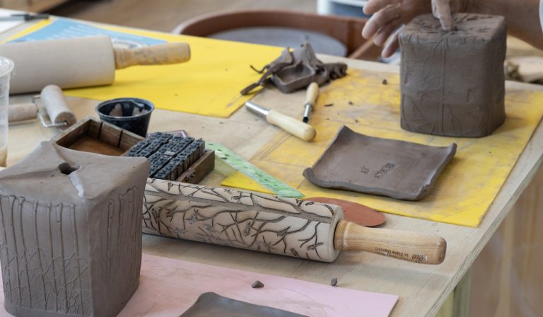 A work table with clay, rolling pins, and tools to make clay pots.