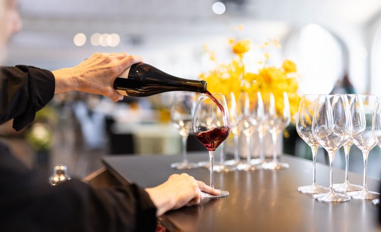 A person behind a bar pouring red wine into a glass.