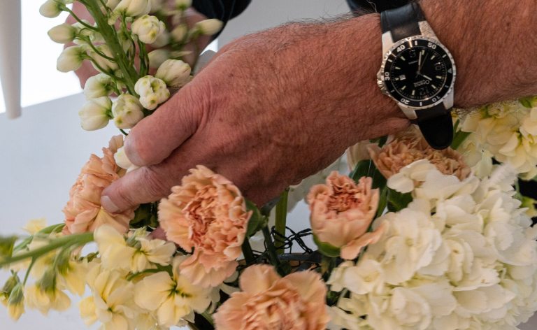 Hands, with a black wrist watch, working with a floral arrangement.