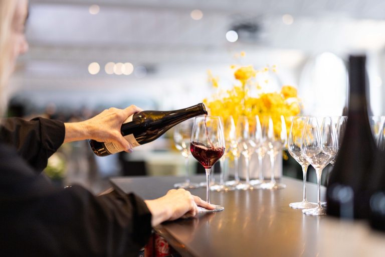 A person behind a bar pouring red wine into a glass.
