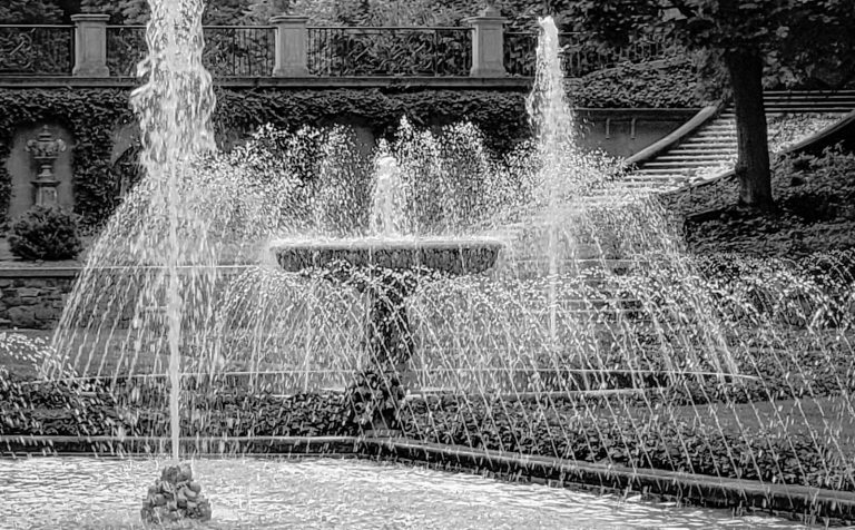 A black and white image of Italian inspired fountains in an outdoor garden.